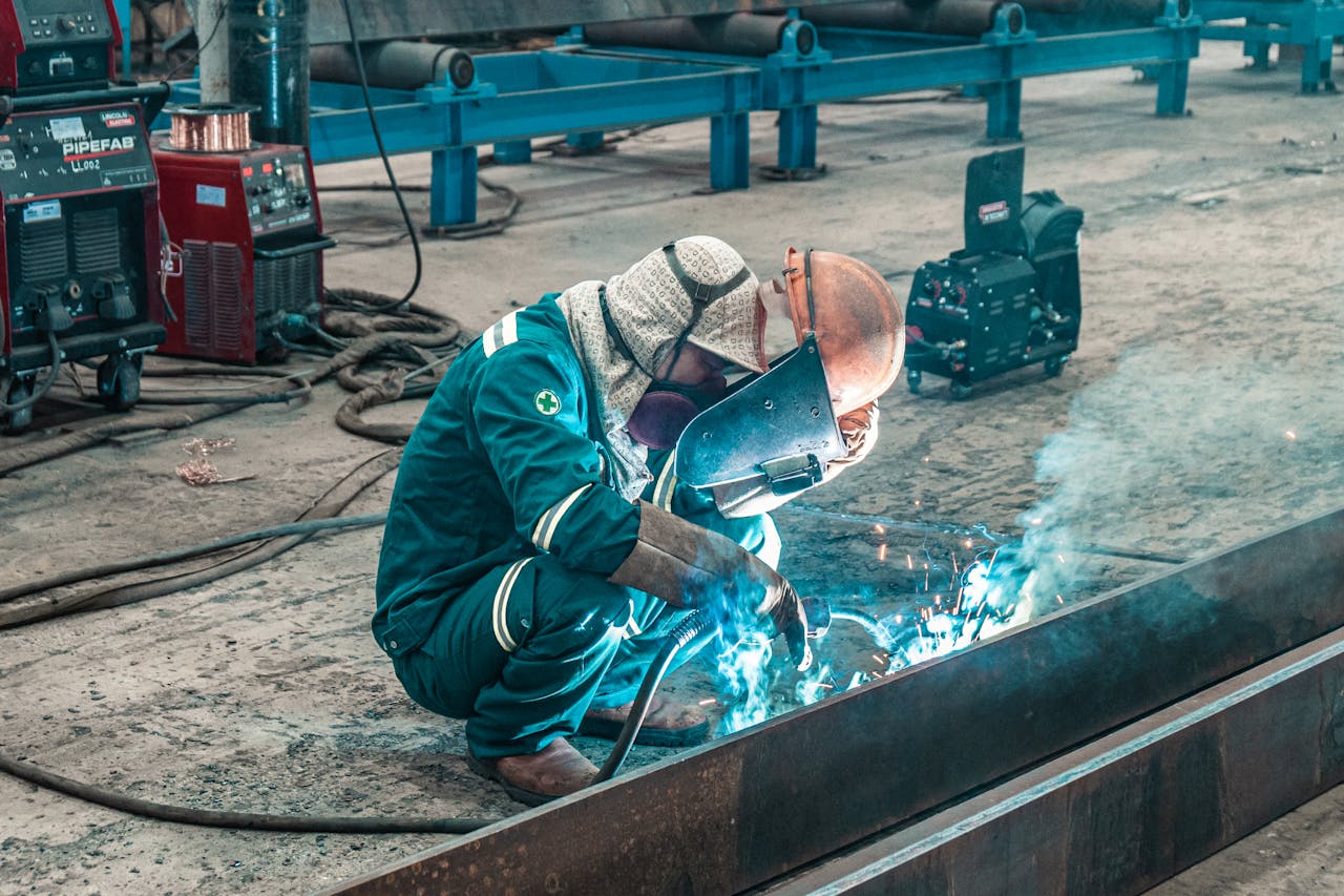 A welder using protective gear works on metal in a factory workshop.